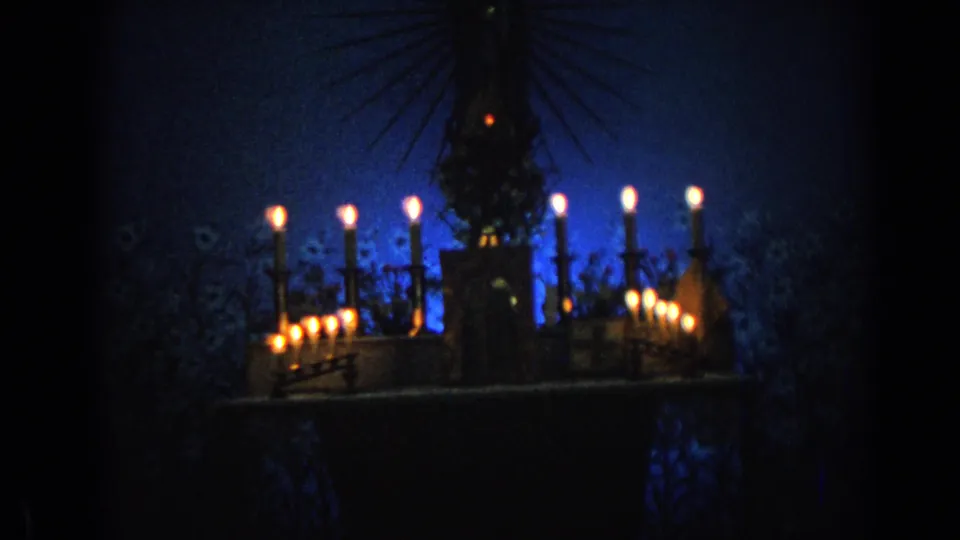 1962 Izmir 8mm frame of a candlelit Marian display, with a dark statue form centered above rows of flames.
