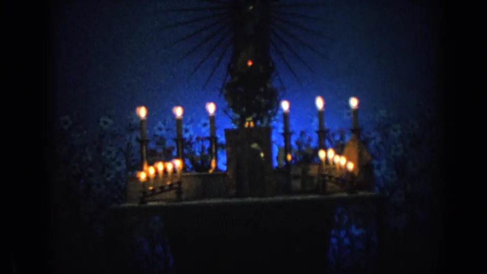 1962 Izmir 8mm frame showing a haloed religious statue and clustered candles glowing in a dark blue nighttime scene.