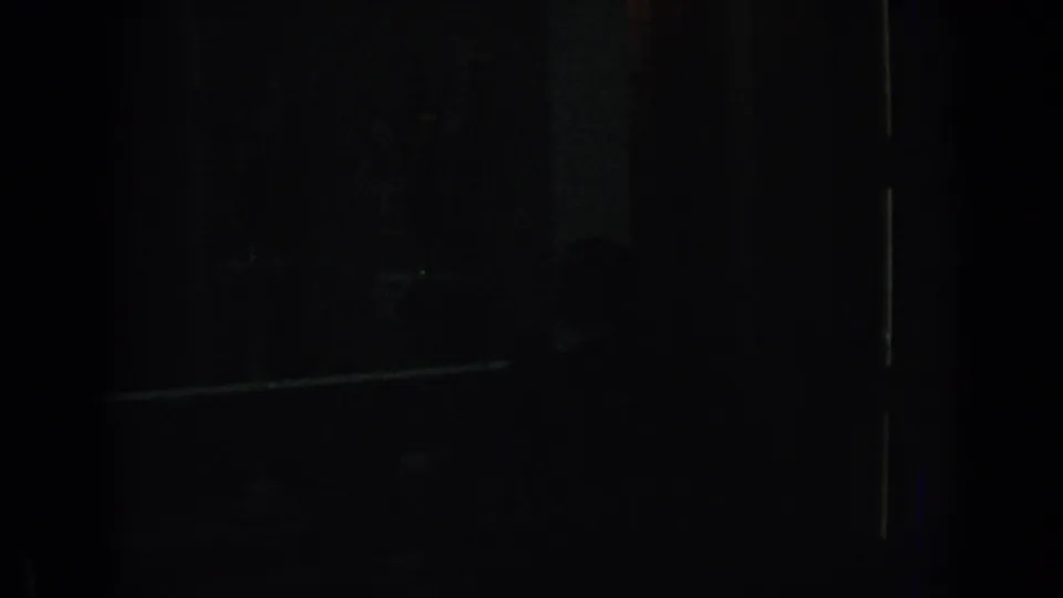 Underexposed 1962 Izmir home-movie frame showing a nearly black private interior with faint structural lines and possible shadow forms.