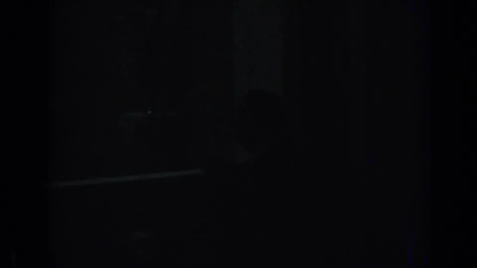 Shadowed 8mm frame from Izmir, 1962, with a barely visible human silhouette and a pale horizontal streak in the darkness.