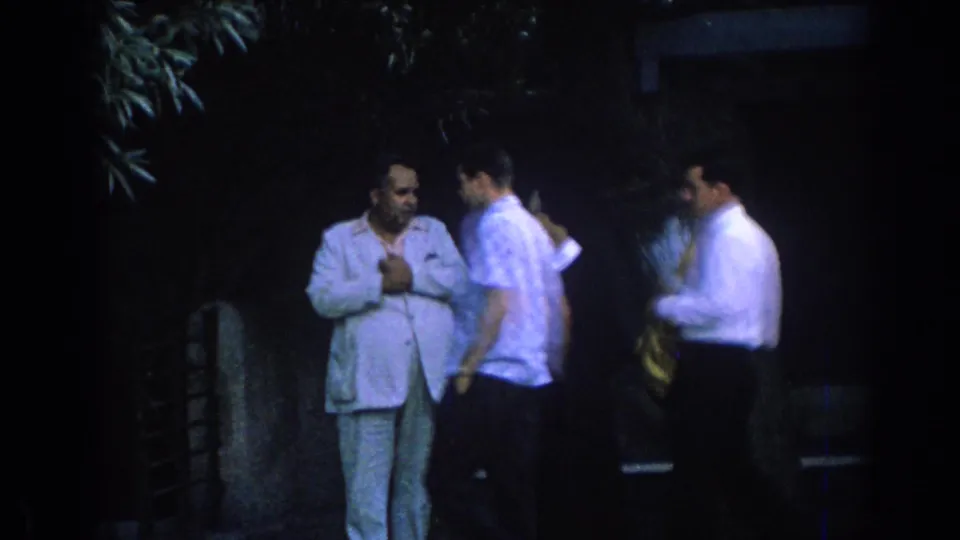 1962 Izmir frame showing two young men passing a suited man and woman, with one carrying a yellow jacket.
