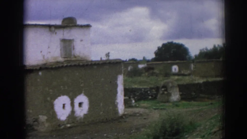 1962 Izmir-area frame with a closer view of a weathered earthen building, small white-painted openings, low roof, and rural greenery.