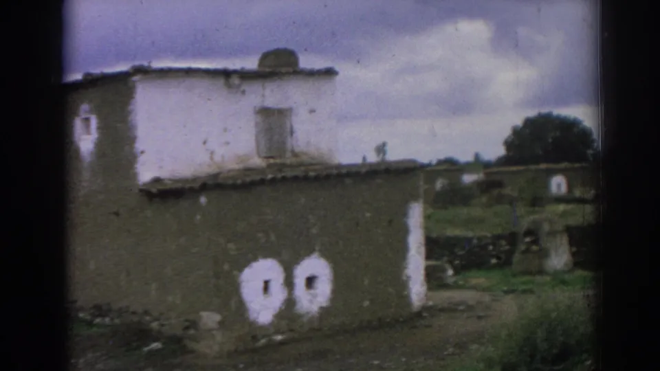1962 Izmir-area 8mm frame showing a worn wall, white-edged openings, a pale upper building section, and grass at the side.