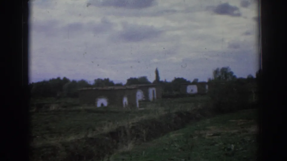 1962 Izmir frame with low abandoned structures, pale arched openings, trees, and uneven grassy terrain.
