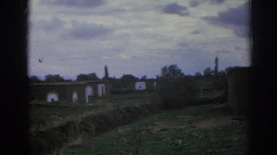 1962 Izmir home-movie view of distant stone structures, arched openings, a grassy bank, and overcast sky.