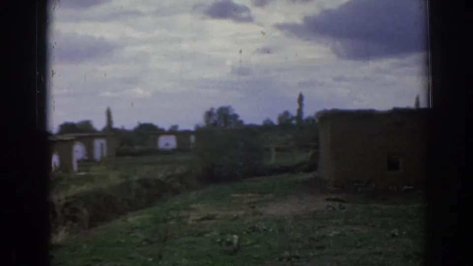 1962 Izmir frame showing a plain foreground building, grassy terrain, and distant abandoned rural structures.