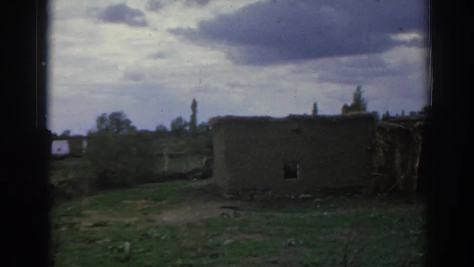 1962 Izmir, Turkey frame with a low mud-brick-looking structure, open land, distant trees, and overcast sky.