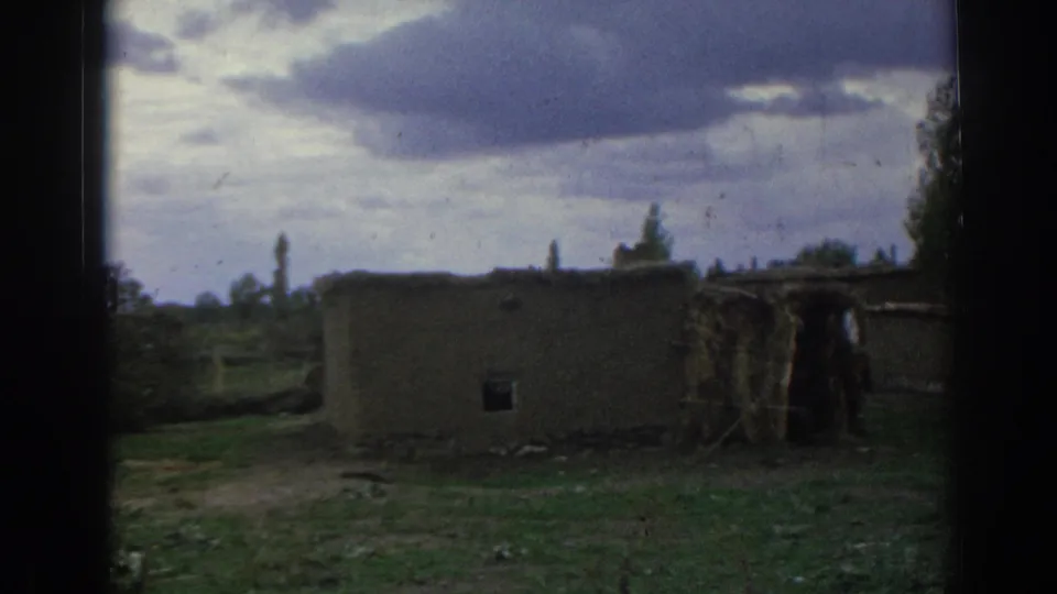 1962 Izmir, Turkey home-movie view of a low rural structure with debris and rough ground beneath an overcast sky.