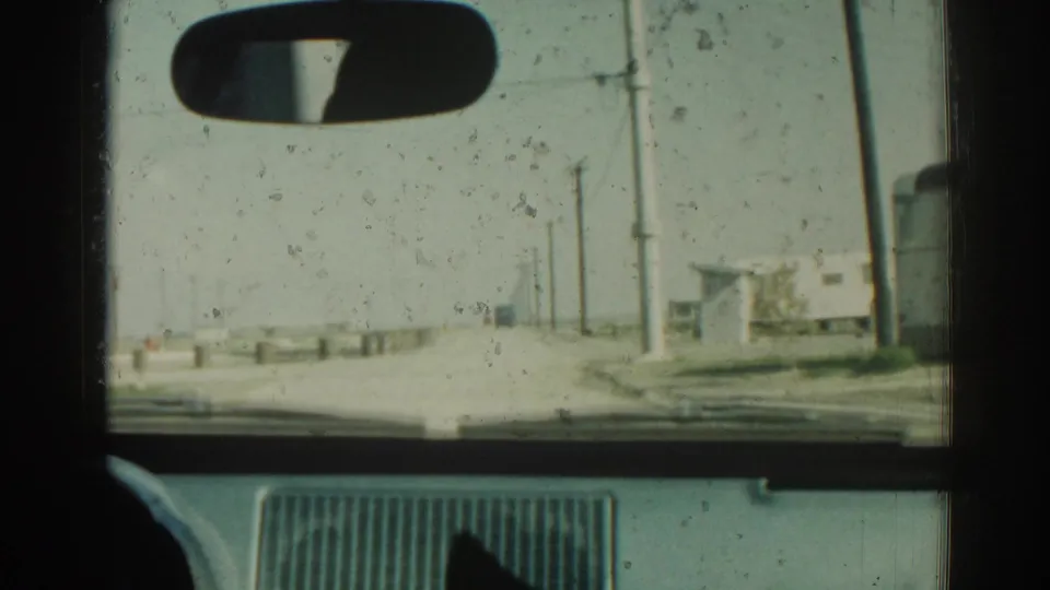 1962 Izmir, Turkey travel frame from inside a vehicle, showing the dashboard, rearview mirror, dusty road, and utility poles.