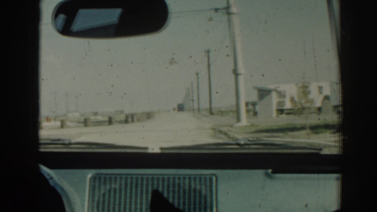 View through a car windshield toward a quiet road with roadside poles and a small white building.