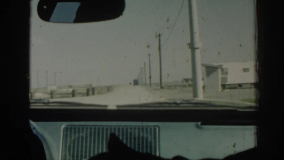 In-car 1962 Izmir road view with the mirror and dashboard framing a sparse roadside landscape.