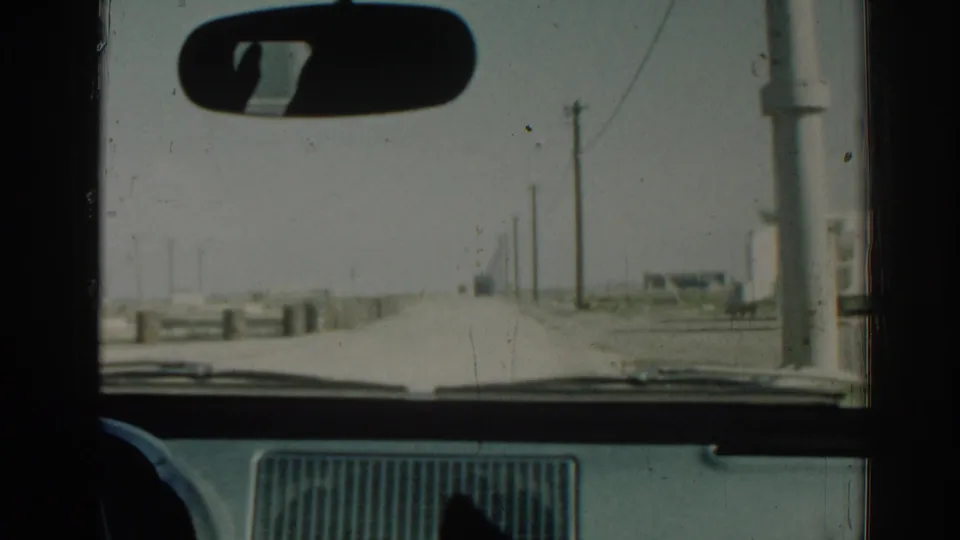 1962 Izmir windshield shot from a moving car, with dashboard, mirror, roadside poles and a low barrier visible.