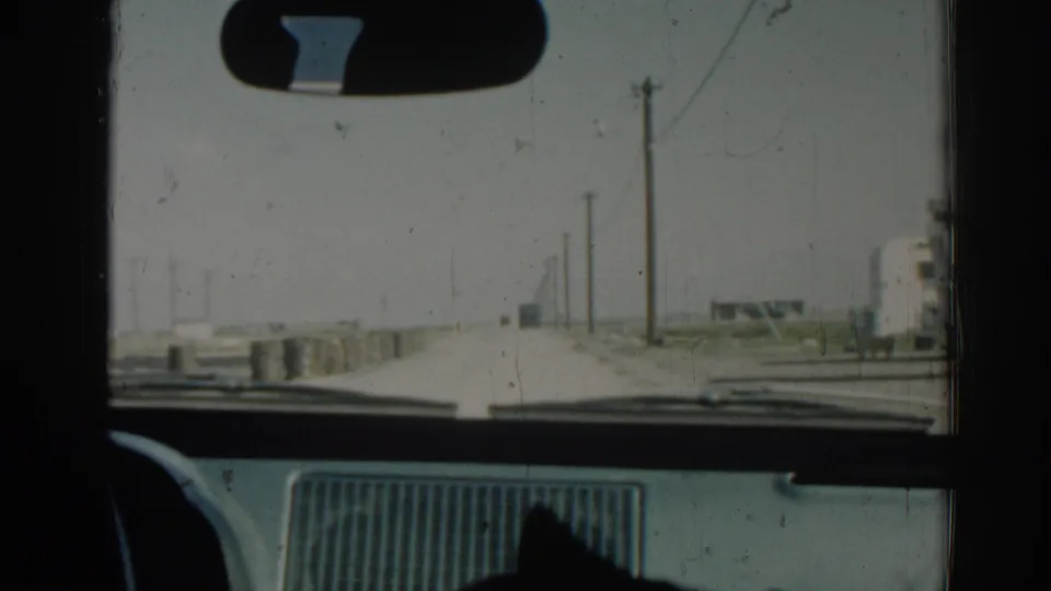 Late frame of the 1962 Izmir drive, showing the car interior framing a quiet road with utility poles and barriers.
