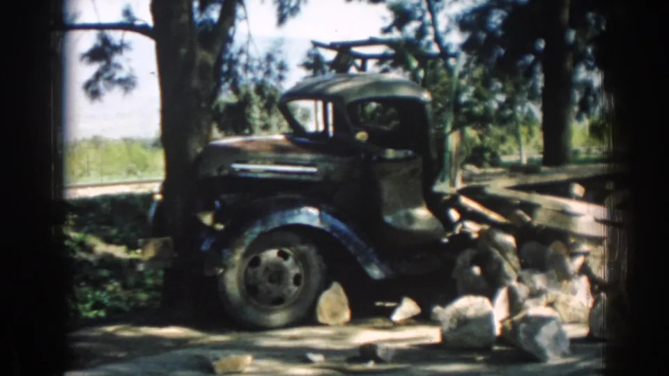 The shot holds on the side of an older parked truck beneath trees, continuing the 1962 Izmir transport cutaway.