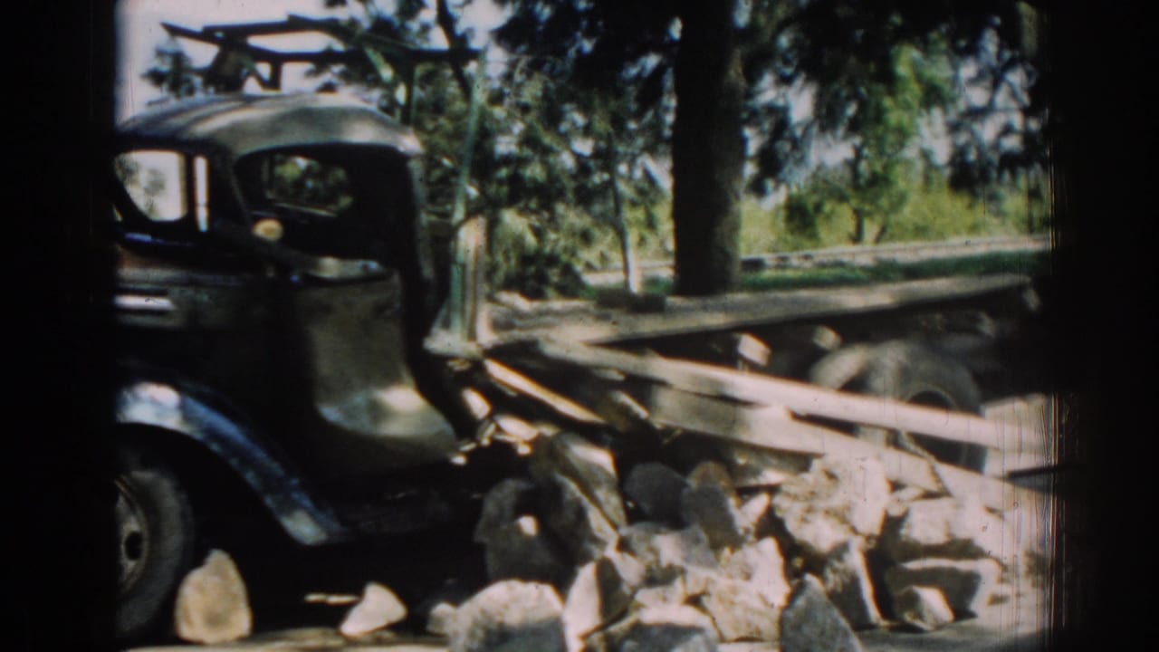 1962 Izmir home-movie frame showing a dark truck cab and wooden flatbed stopped beside scattered roadside rocks.