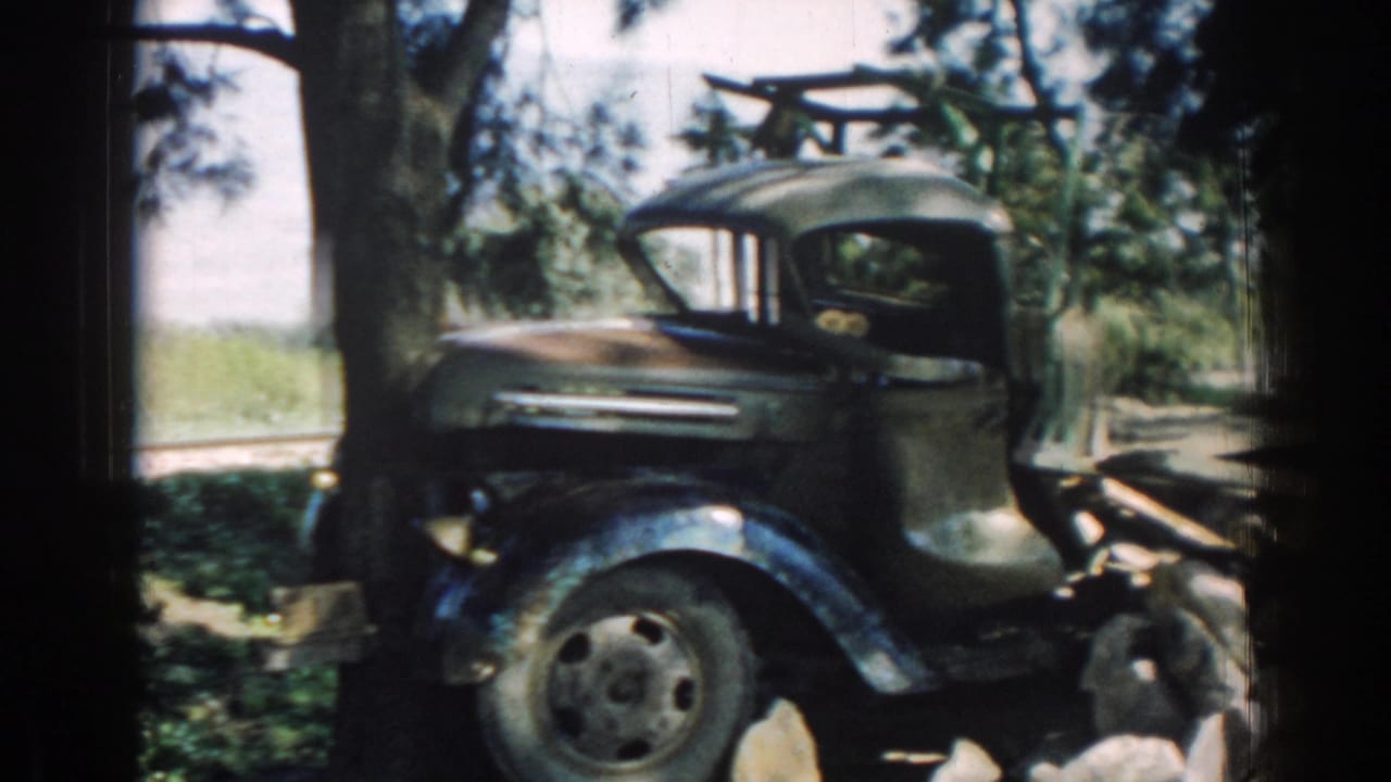 Side view of an older truck cab near roadside rocks and trees.