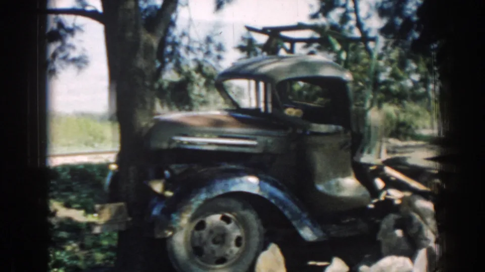 Older dark truck cab near a tree-lined roadside in Izmir, with rocks and part of the flatbed visible.