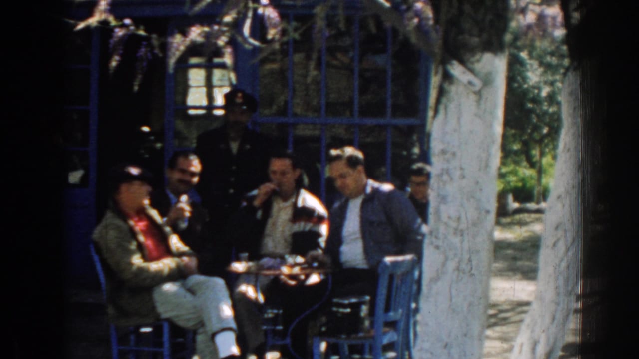 Men seated around a small outdoor table beside a blue-painted building.