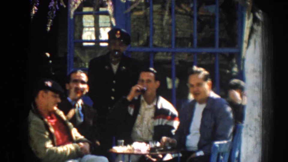 In the Izmir 1962 footage, one man drinks from a small glass while companions sit around a table beneath blue window bars.