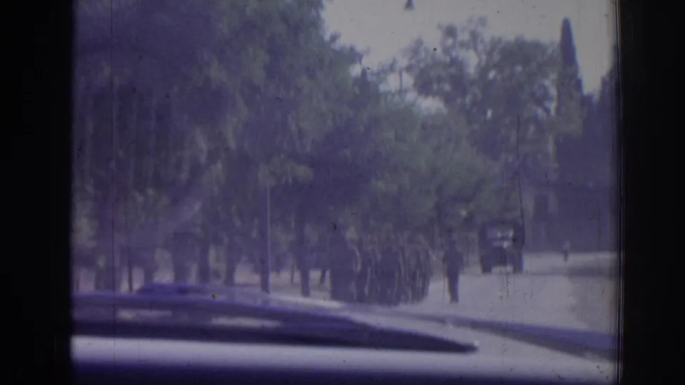 Inside-car 8mm view in Izmir, Turkey, showing uniformed soldiers marching along a tree-lined road in 1962.