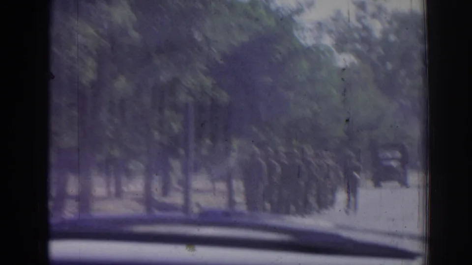 1962 Izmir roadside scene from a moving car, with a line of soldiers marching near trees and a truck ahead.