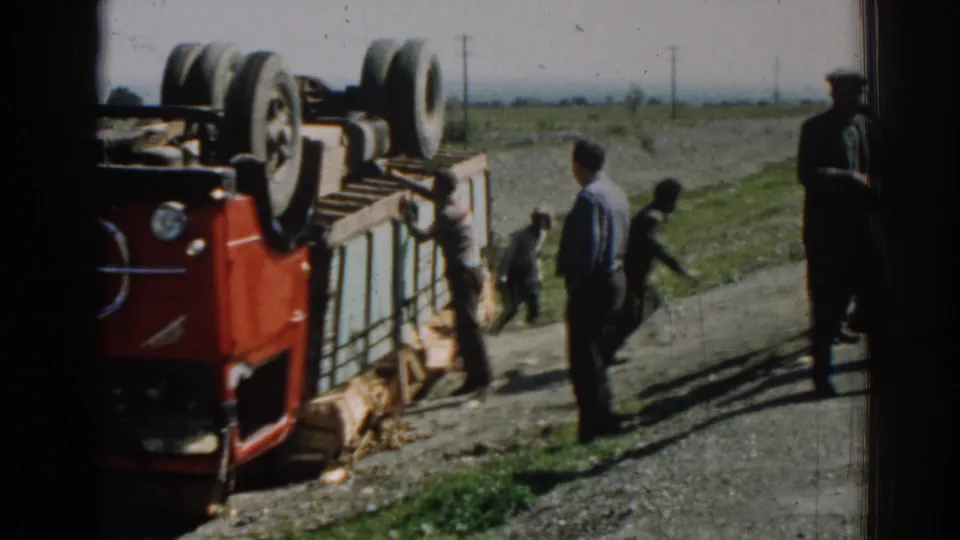 Izmir, Turkey, 1962 frame showing an overturned red truck, spilled cargo, and adult men gathered on a rural road under bright daylight.