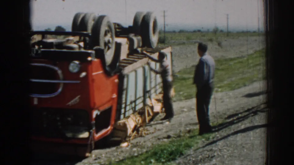 Izmir, Turkey, 1962 frame with a closer view of the overturned red truck as men stand beside the vehicle and spilled material on the road shoulder.
