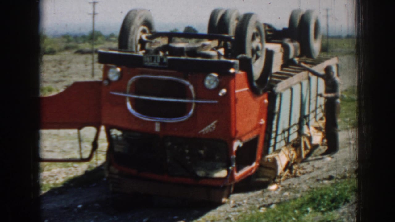 Overturned red and light-blue truck beside a rural road with wheels facing upward.