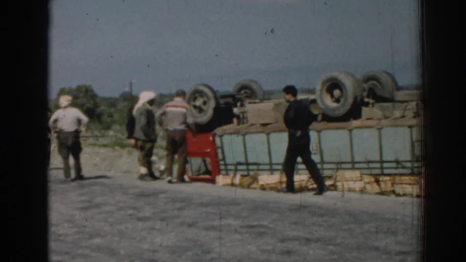 1962 Izmir frame showing men in period clothing moving around the side of an overturned cargo truck on a rural roadside.