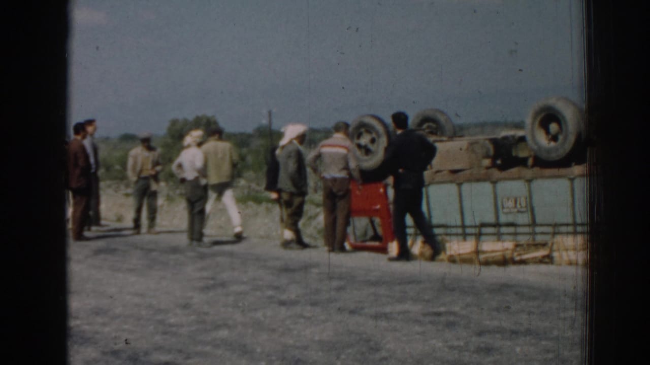 In 1962 Izmir, Turkey, several adult men gather near an overturned red truck on a rural roadside.