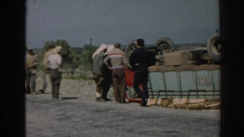 Adult men in period clothing stand beside the flipped red truck in the Izmir roadside accident footage.
