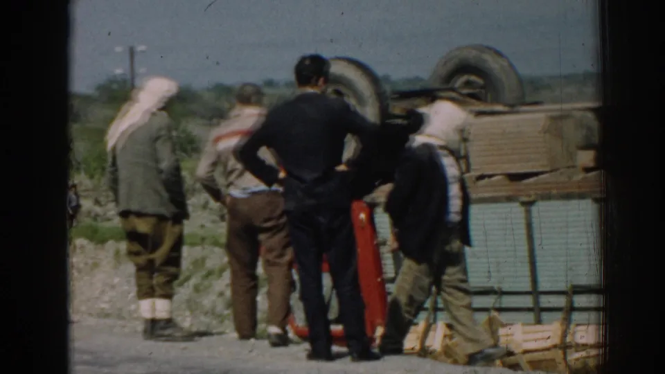 A closer 8mm view shows men inspecting the overturned red truck along a rural road in Izmir.