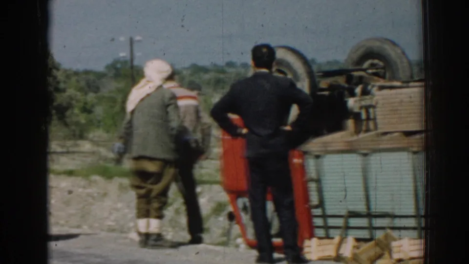 The final frame holds on men near the flipped red truck, with rural trees and a utility pole behind them.