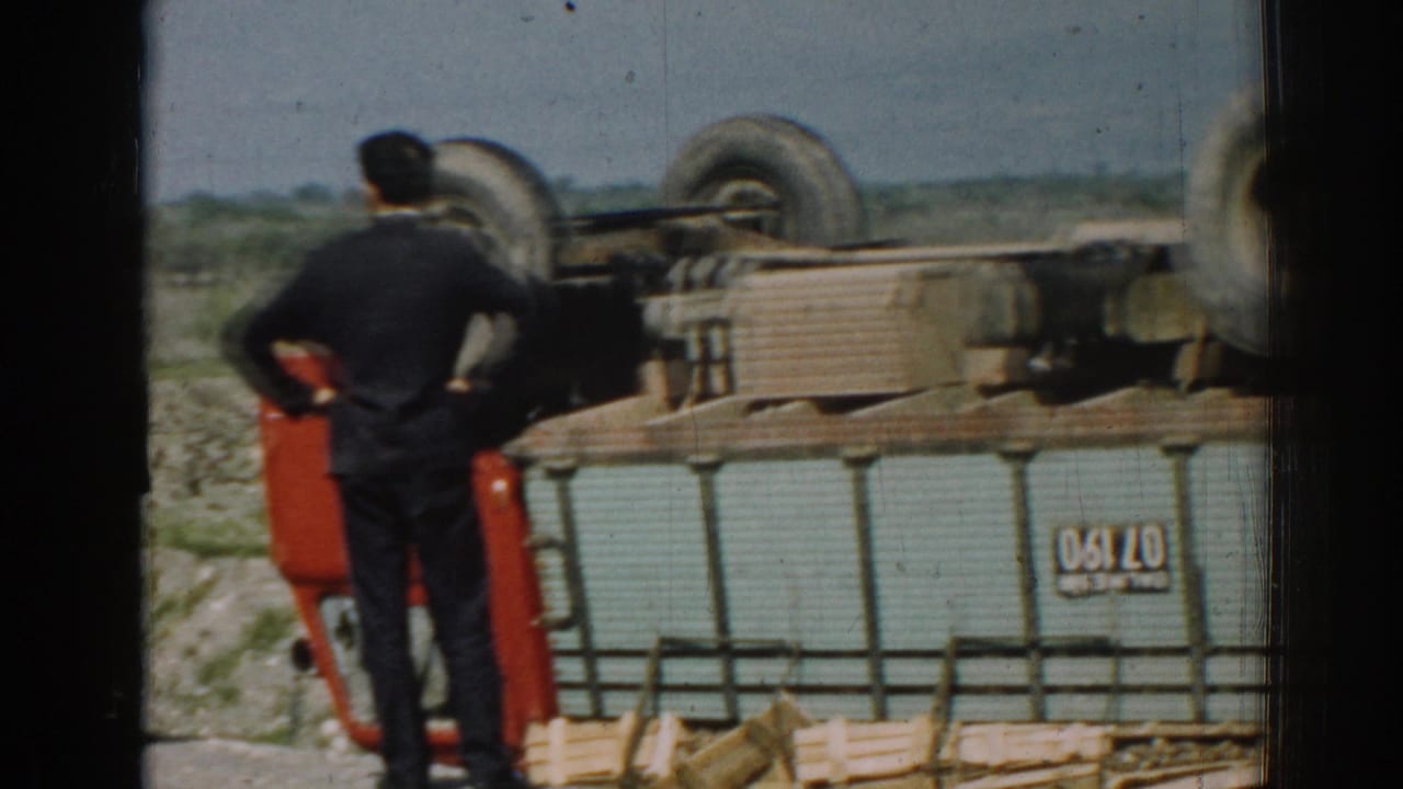 In supported 1962 Izmir footage, a man in dark clothing watches an overturned truck lying on its side near scattered wooden cargo.