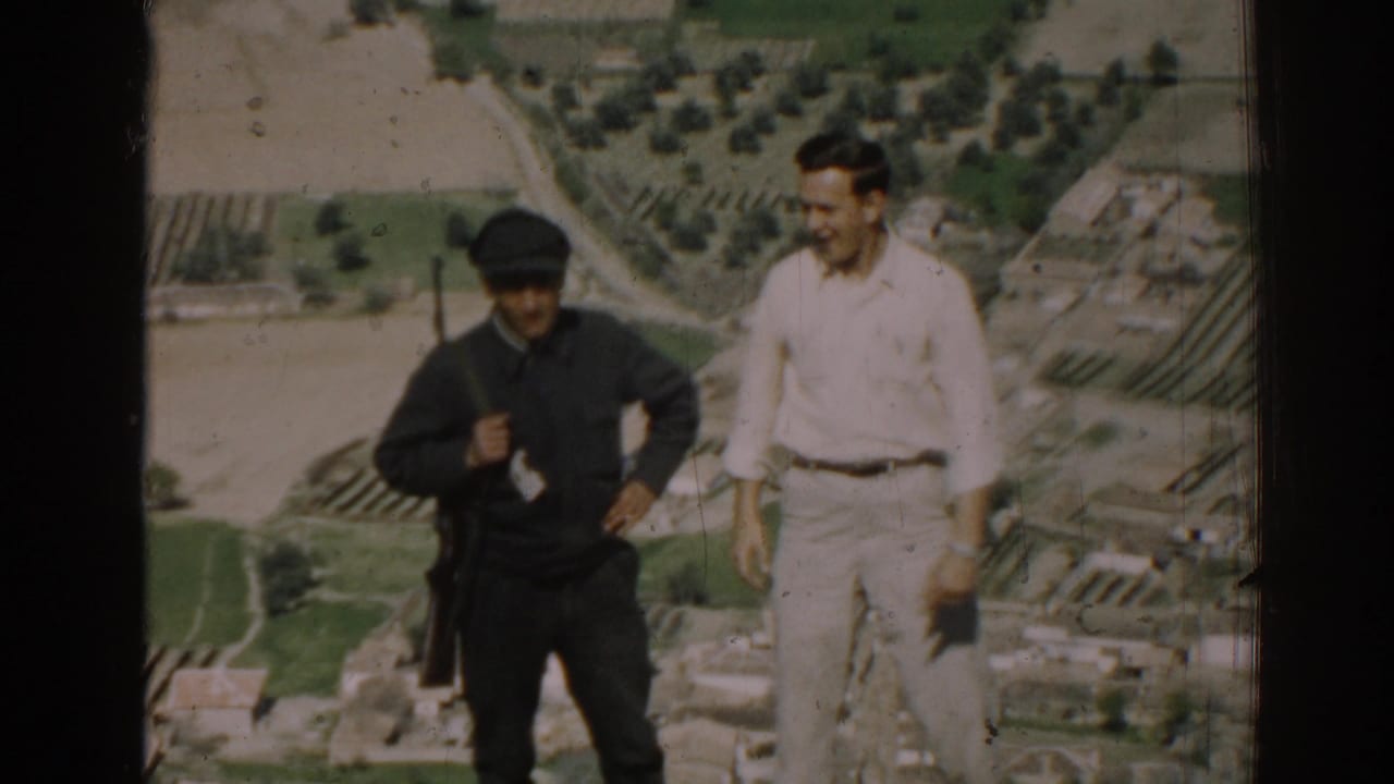 In 1962 Izmir, Turkey, a uniformed man with a rifle stands beside a civilian on a hill above fields and buildings.
