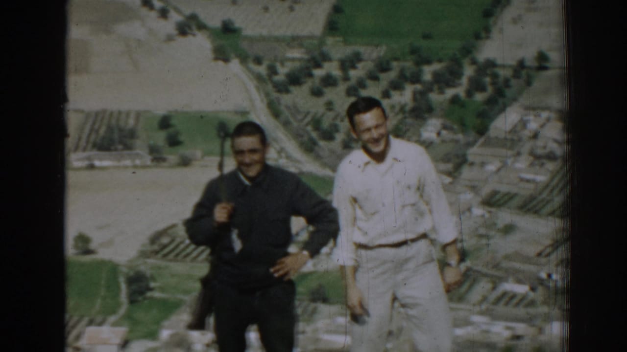 Two men smiling on a hillside above patchwork farmland.