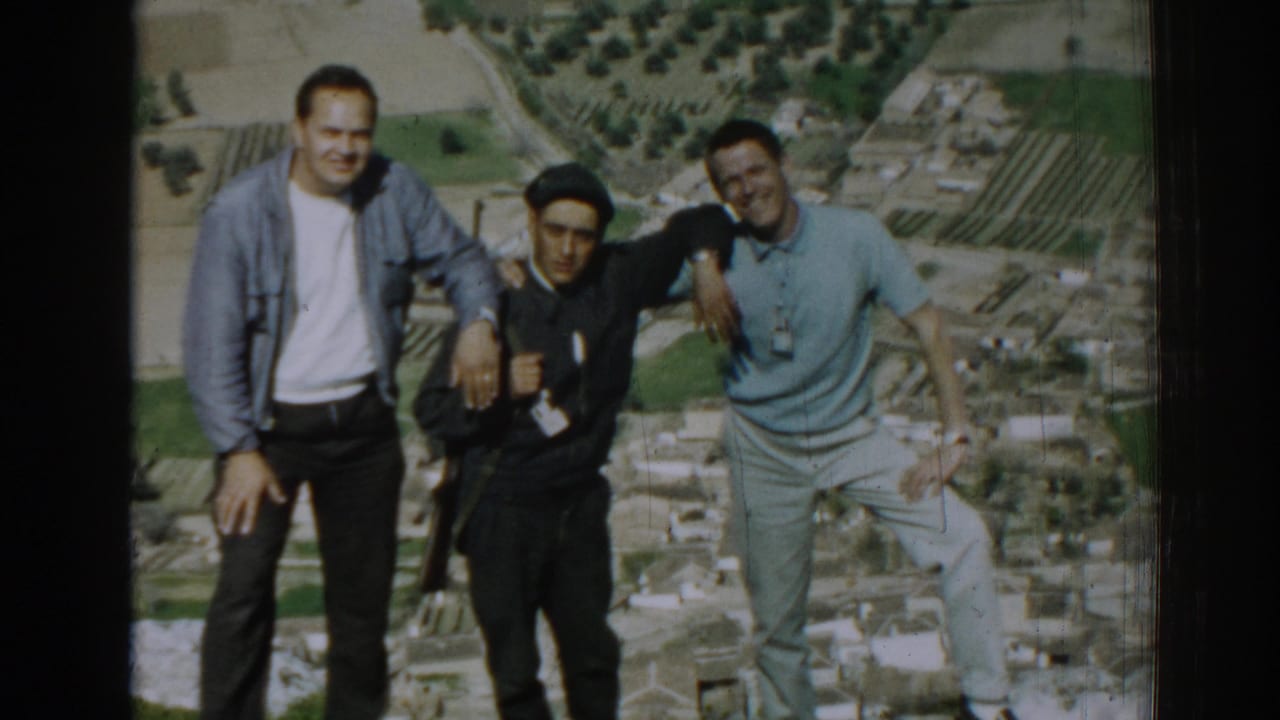 Three young men pose together on a hillside above farmland.