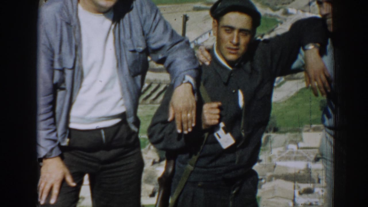 In 1962 Izmir, Turkey, three adult men pose on a sunny elevated site, with the central man in dark clothing and cap partly framed by two companions.