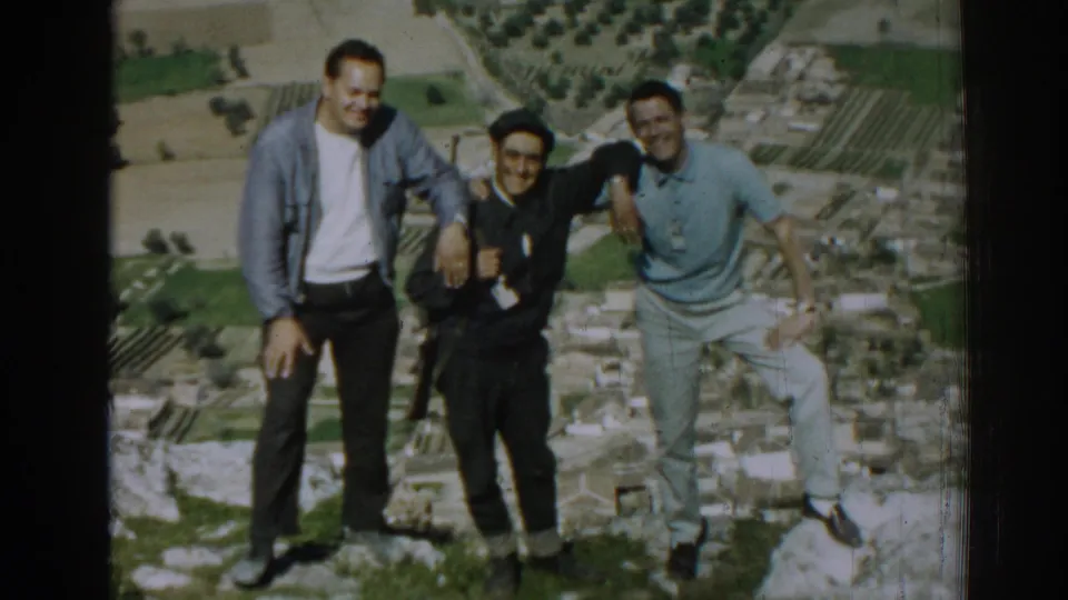 The final frame shows three men standing together in 1962 Izmir, Turkey, on rocky ground above a rural landscape of fields and buildings.