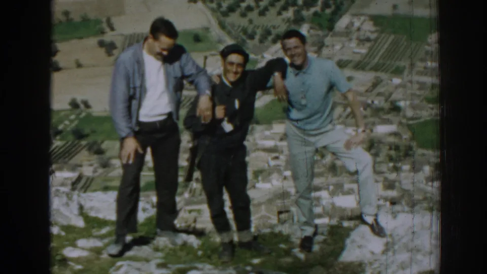 Three adult men pose together on a rocky overlook in Izmir, Turkey, in 1962, with stone ruins and a valley below.