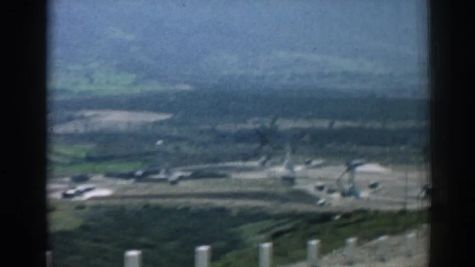 1962 Izmir hillside view with white roadside posts, green slopes, distant buildings, and small vehicles below.