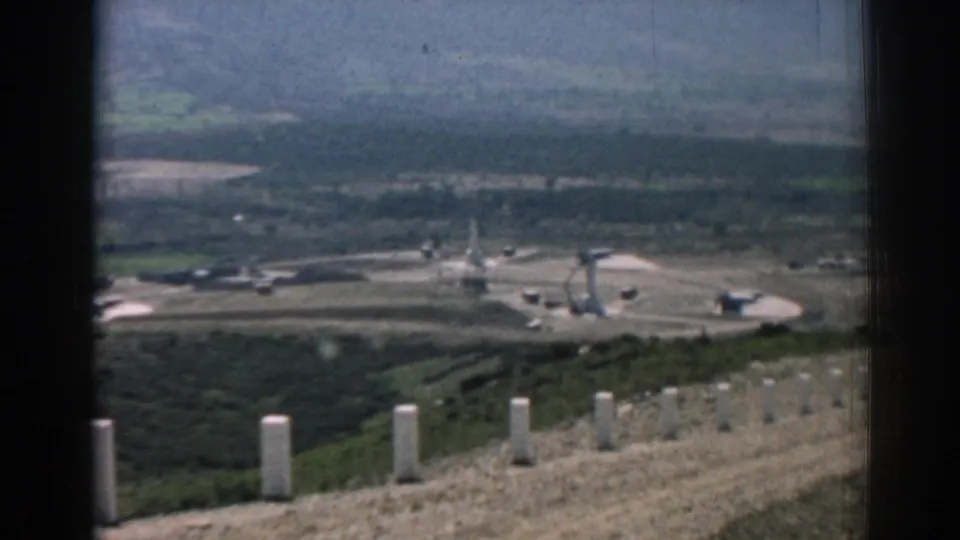 1962 Izmir home-movie frame showing a hillside path with white posts above a broad construction site and distant hills.