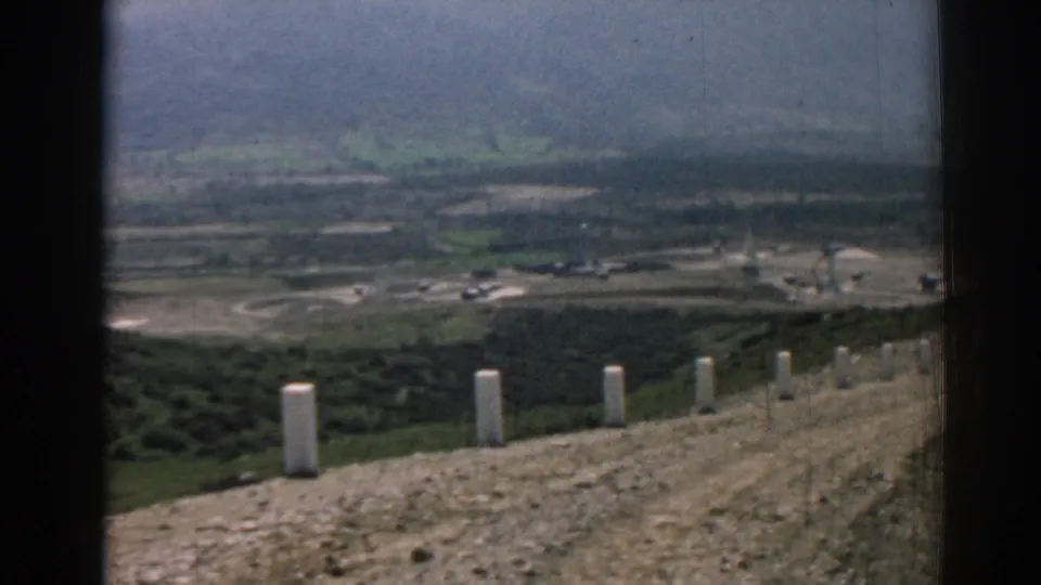 Final 1962 Izmir frame shows a hillside overlook, white roadside posts, scattered buildings, and distant green hills.
