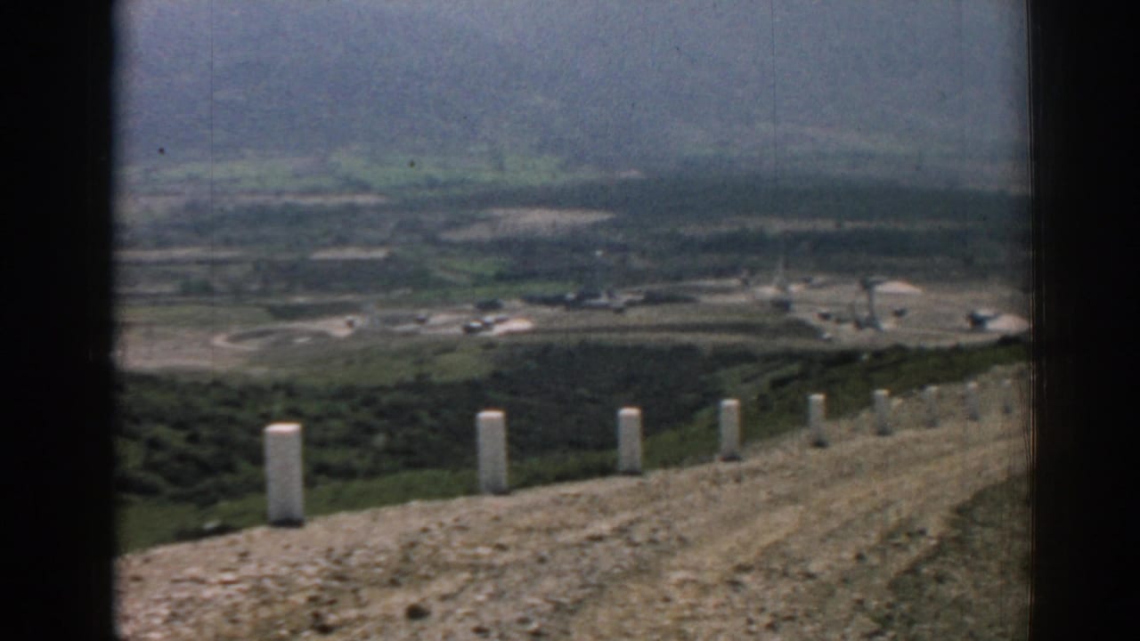 Dirt road on a mountain ridge with white roadside posts above a hazy valley.