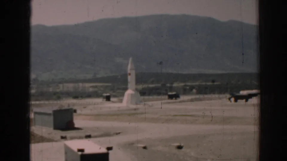 The missile remains centered on the open pad in the 1962 Izmir view, with vehicles, distant hills, and visible 8mm film wear.