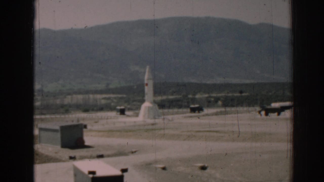 White rocket standing on a paved outdoor pad with hills in the background.