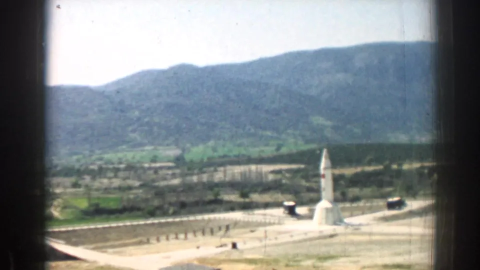 1962 Izmir, Turkey view of a white rocket or missile-like structure on a pad, seen from a window with hills behind it.