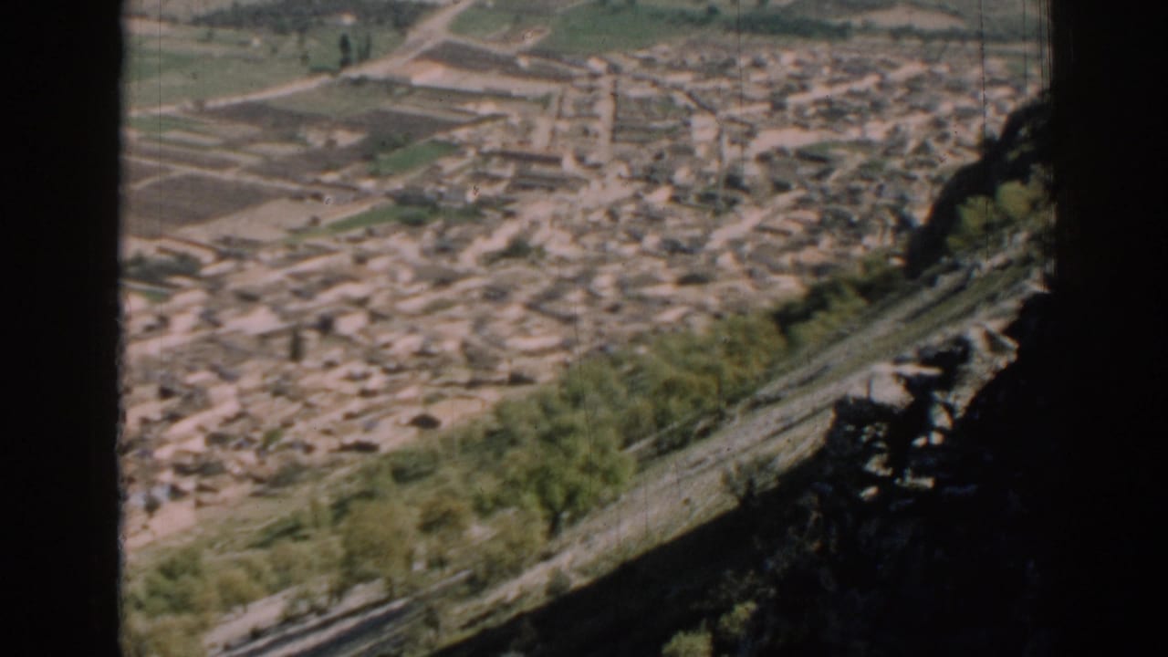 High view over clustered buildings, fields, and hillside trees with dark frame obstruction.