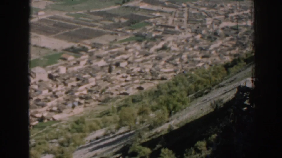 Elevated 1962 Izmir view with dense low-rise buildings, patterned fields, hillside vegetation, and a dark edge at right.