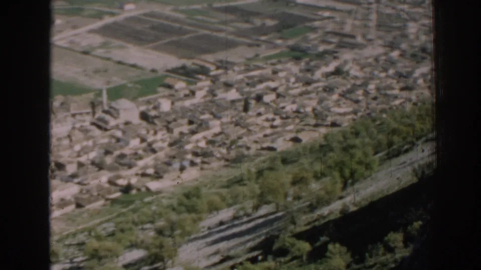 1962 Izmir frame with a tall narrow tower, dense buildings, farm plots, roads, and hillside trees in soft focus.